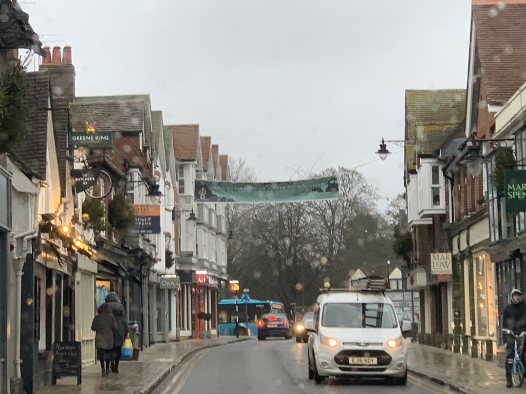 A high street with shops, a pub, pedestrians and passing traffic